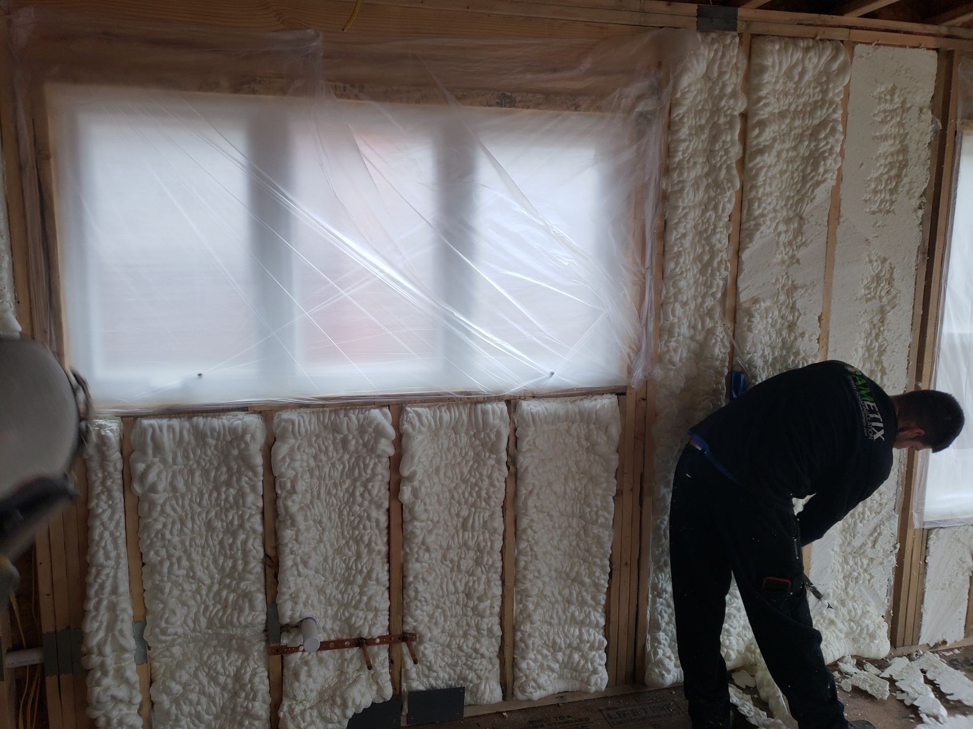 A man is spray foaming a wall in a room.