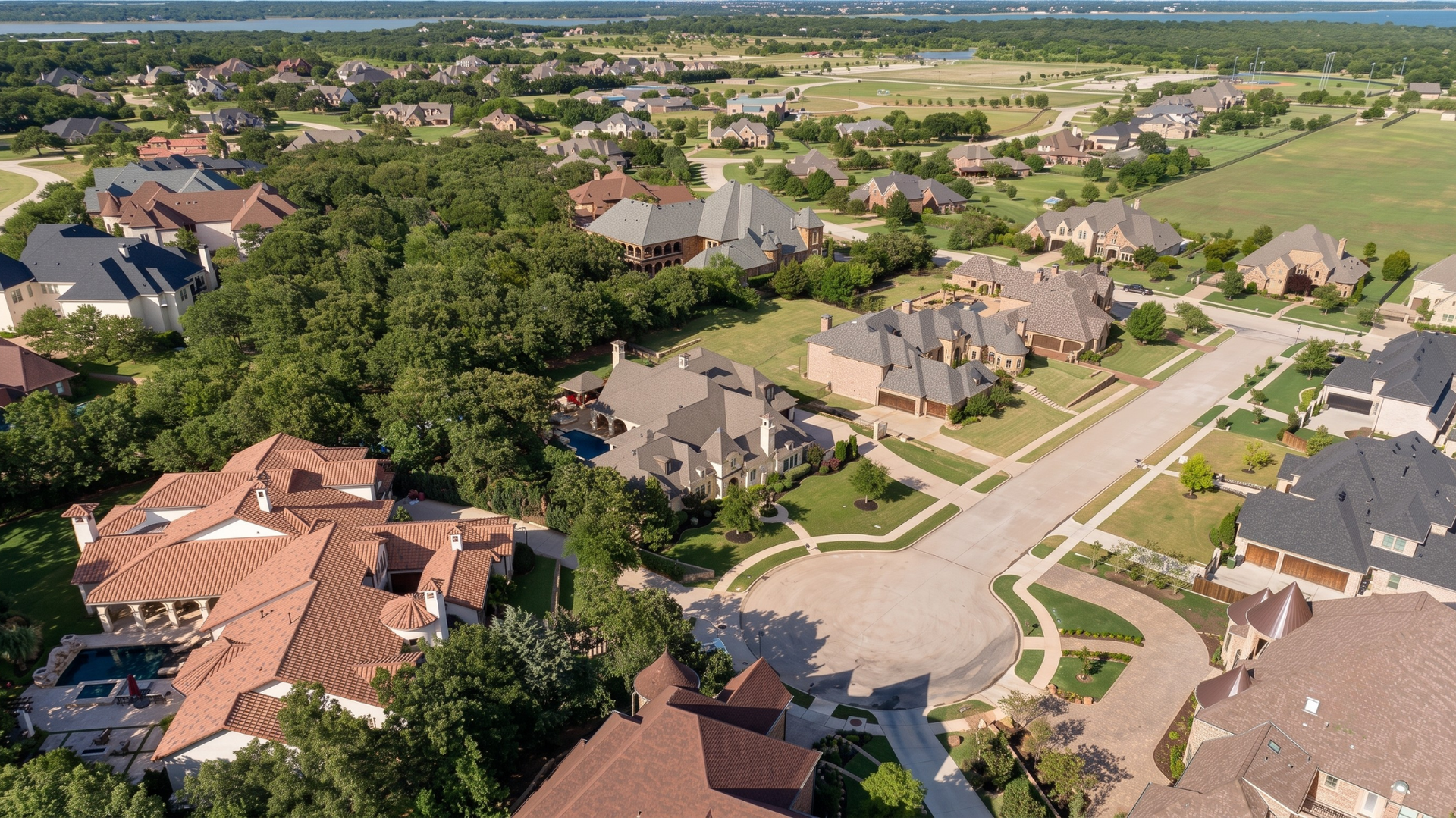 Aerial view of a suburban neighborhood with houses, tree-lined streets, and green open fields.