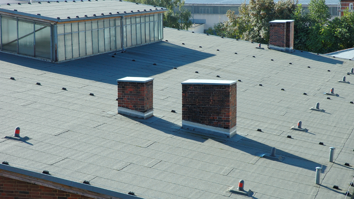 Flat rooftop with two brick chimneys and a ventilation structure under clear daylight.
