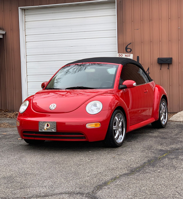 Red Volkswagen Beetle parked in front of a garage door and wooden building.