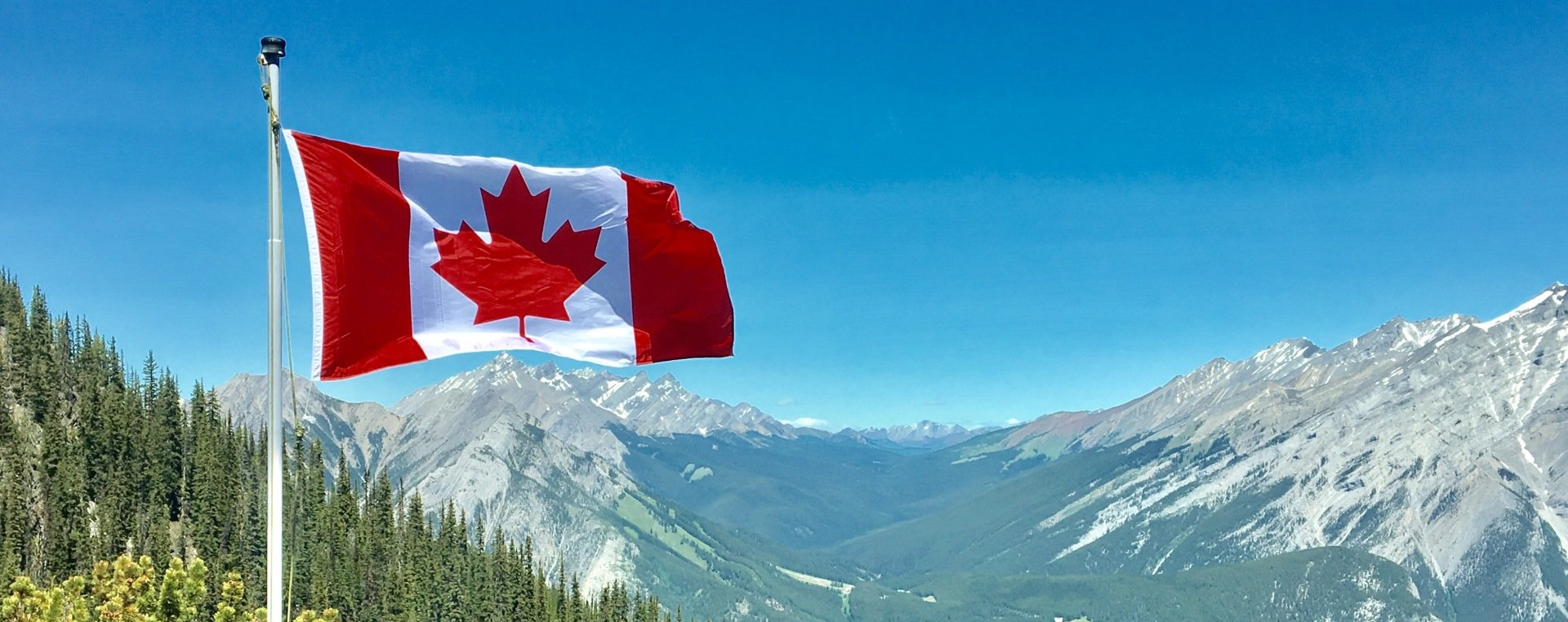 A canadian flag is flying in front of a mountain range.