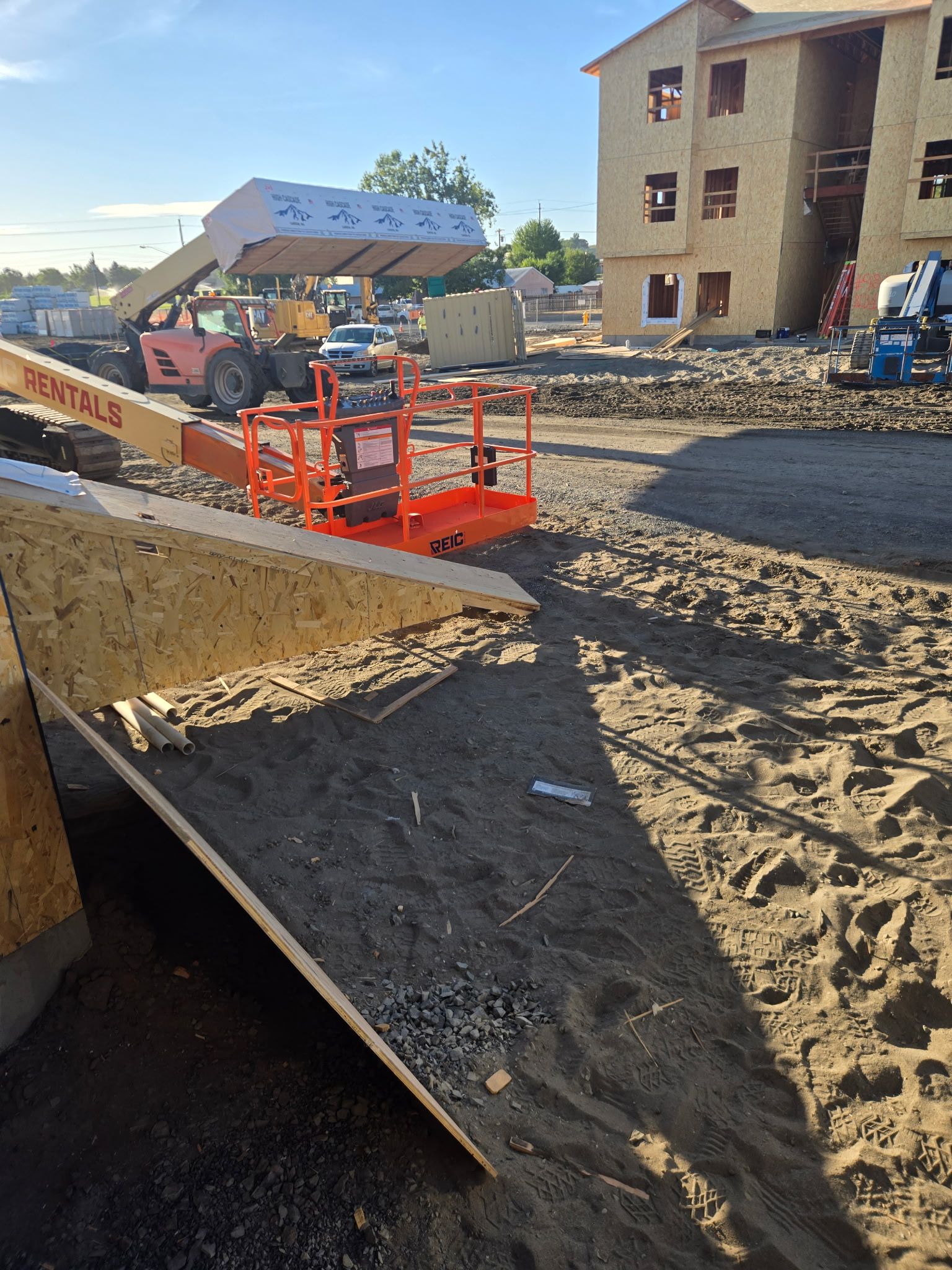 Construction site with orange lift near a building and gravel pile behind a dirt trench