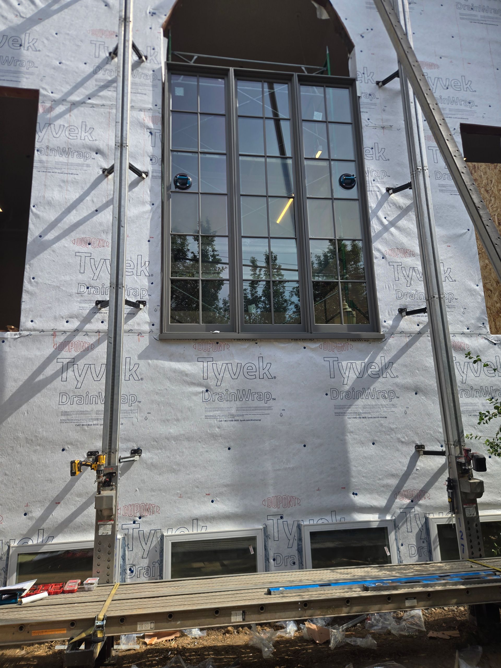 White stucco wall with a large black-framed window, surrounded by scaffolding during construction.