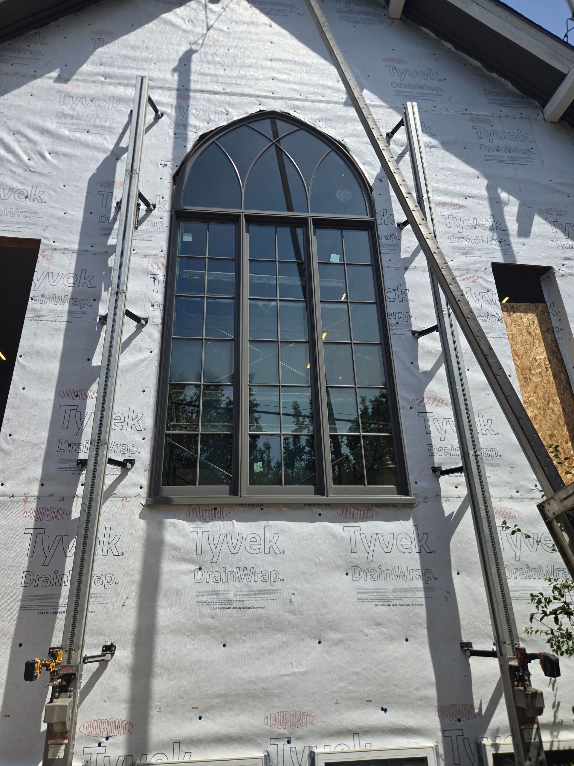White house exterior with large arched window, blue sky reflection, and ladder/scaffolding on both sides