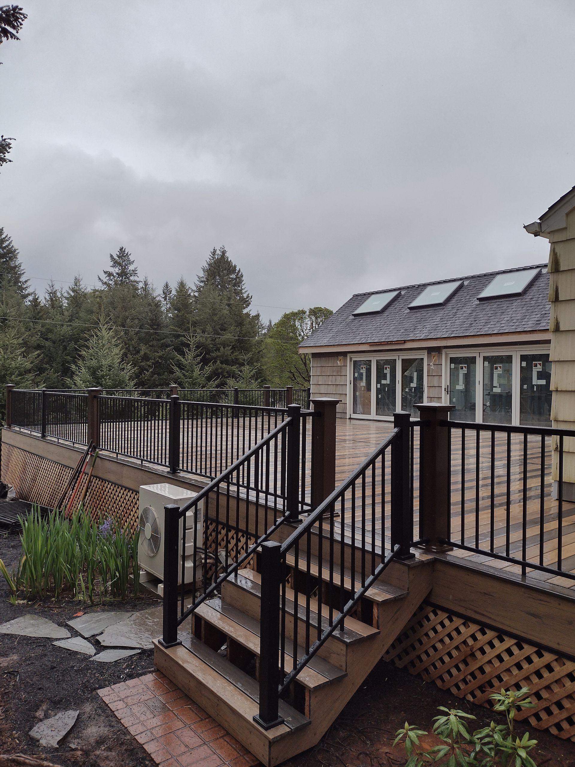 Outdoor stairs and deck with black railings beside a brick building on a rainy day