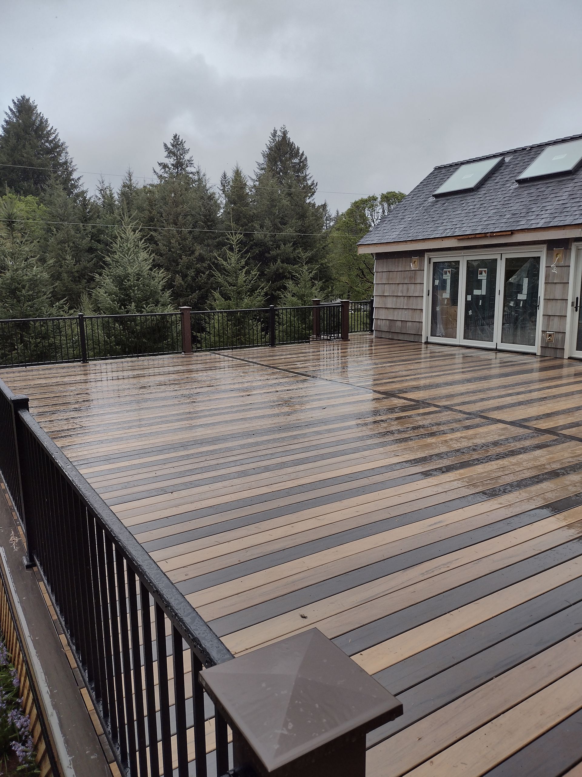 Snow-dusted rooftop deck beside a house, with pine trees in the background