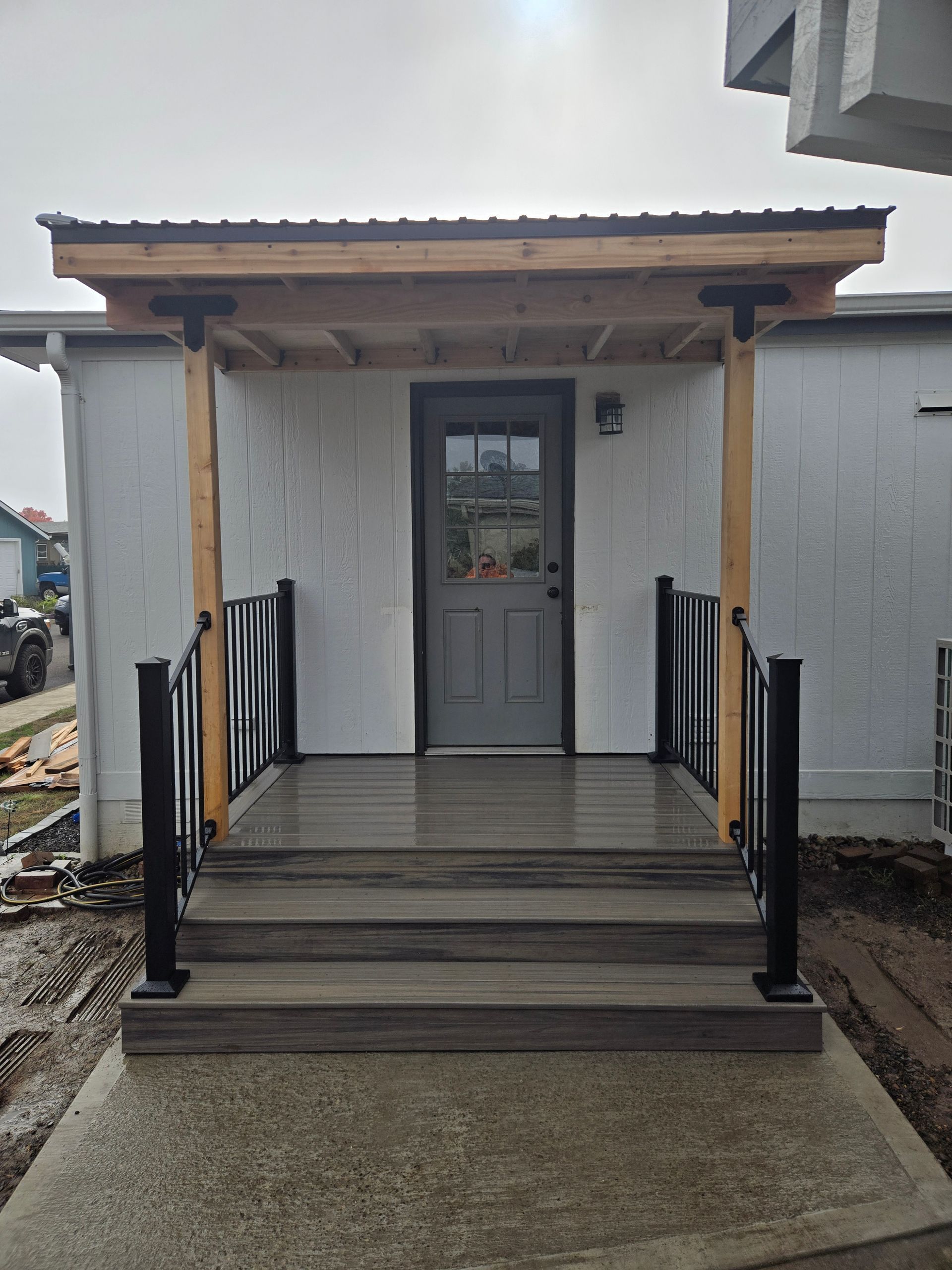 Front porch with steps, black railings, and a gray door on a small white house