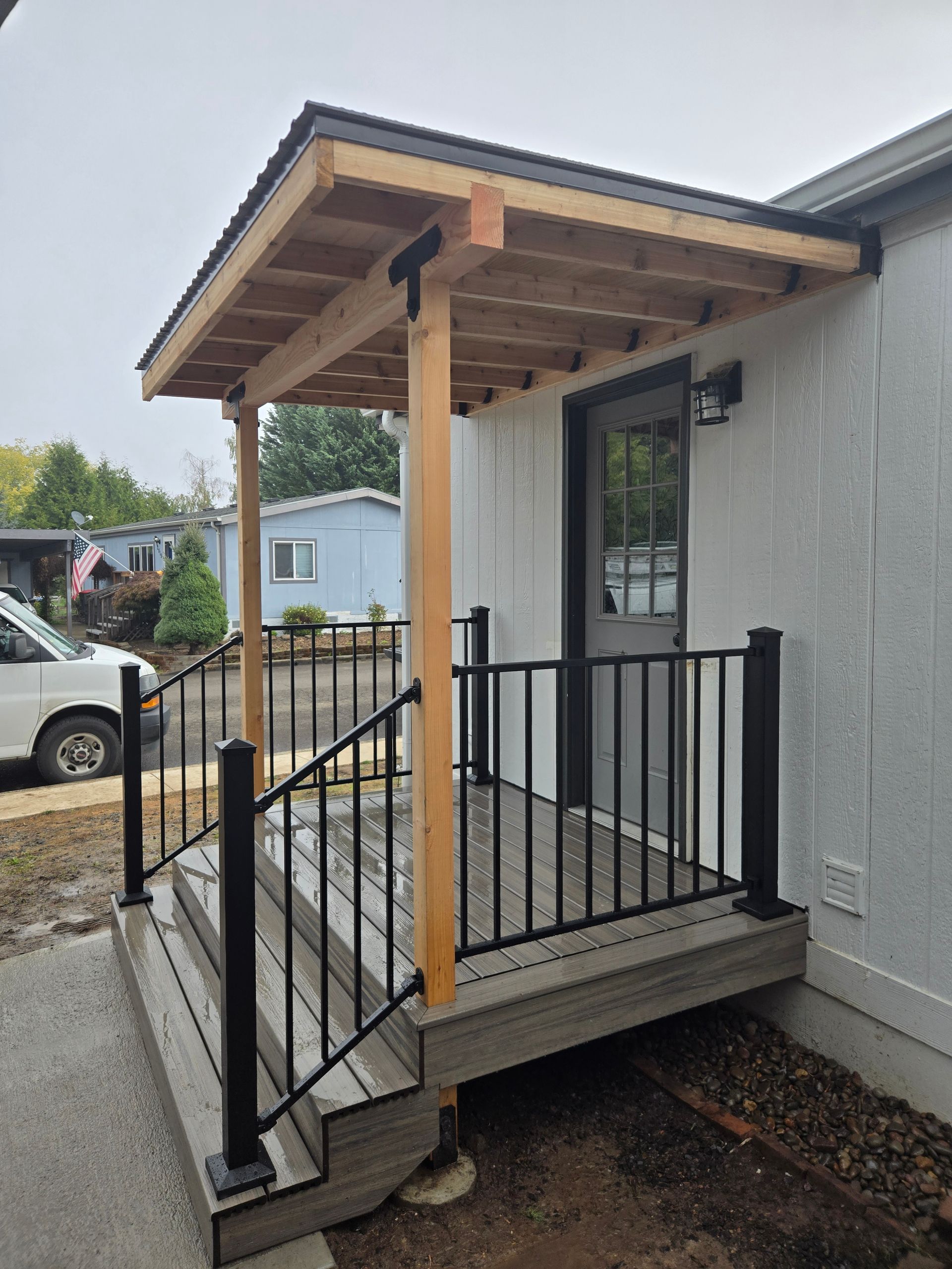 Front porch with black railing and steps, a small wooden roof, and a parked car in the background