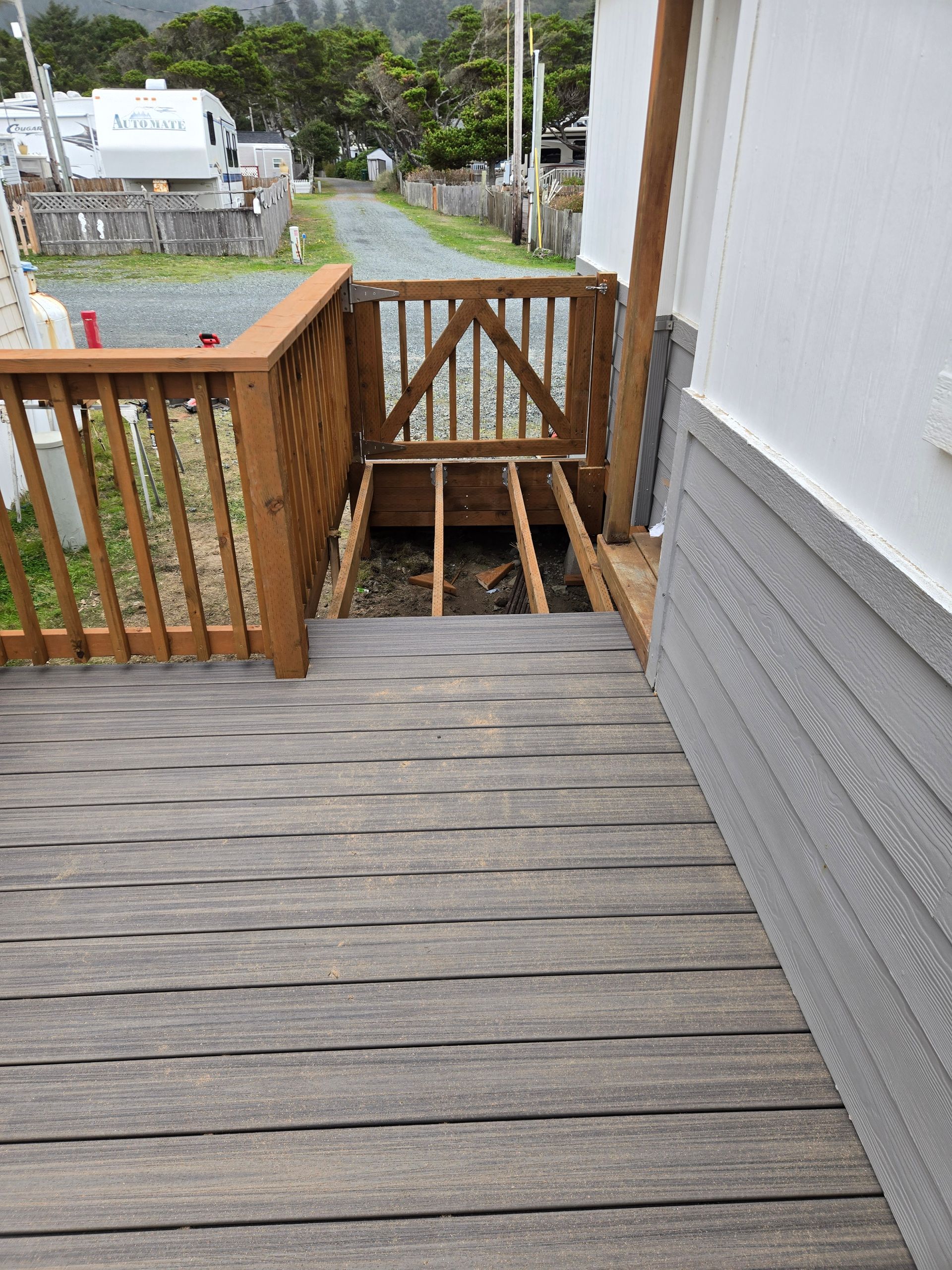 Wooden deck leading to a narrow gate and stairs beside a white and gray house.
