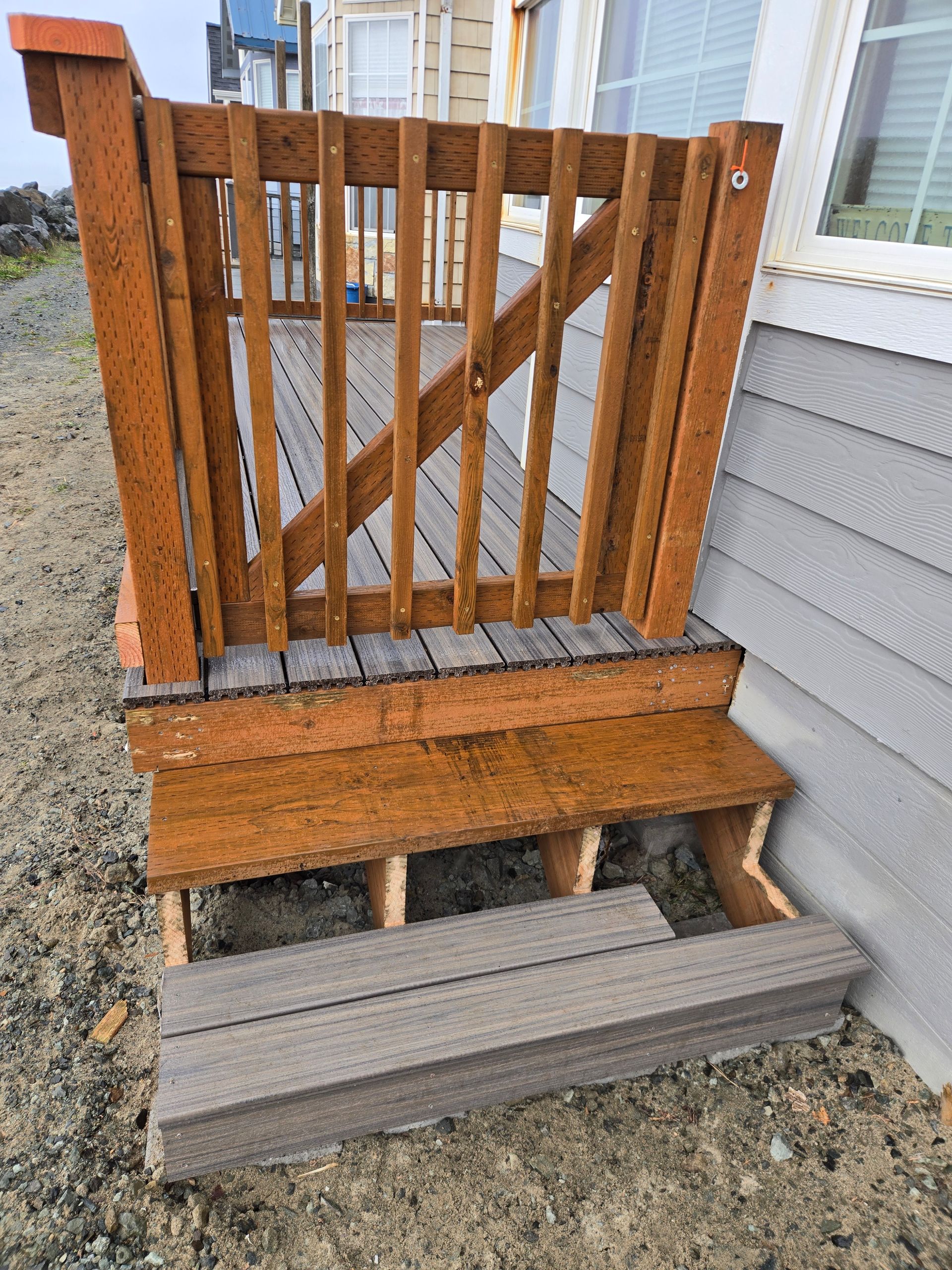 Weathered wooden gate with steps and gray steps leading up beside a house exterior
