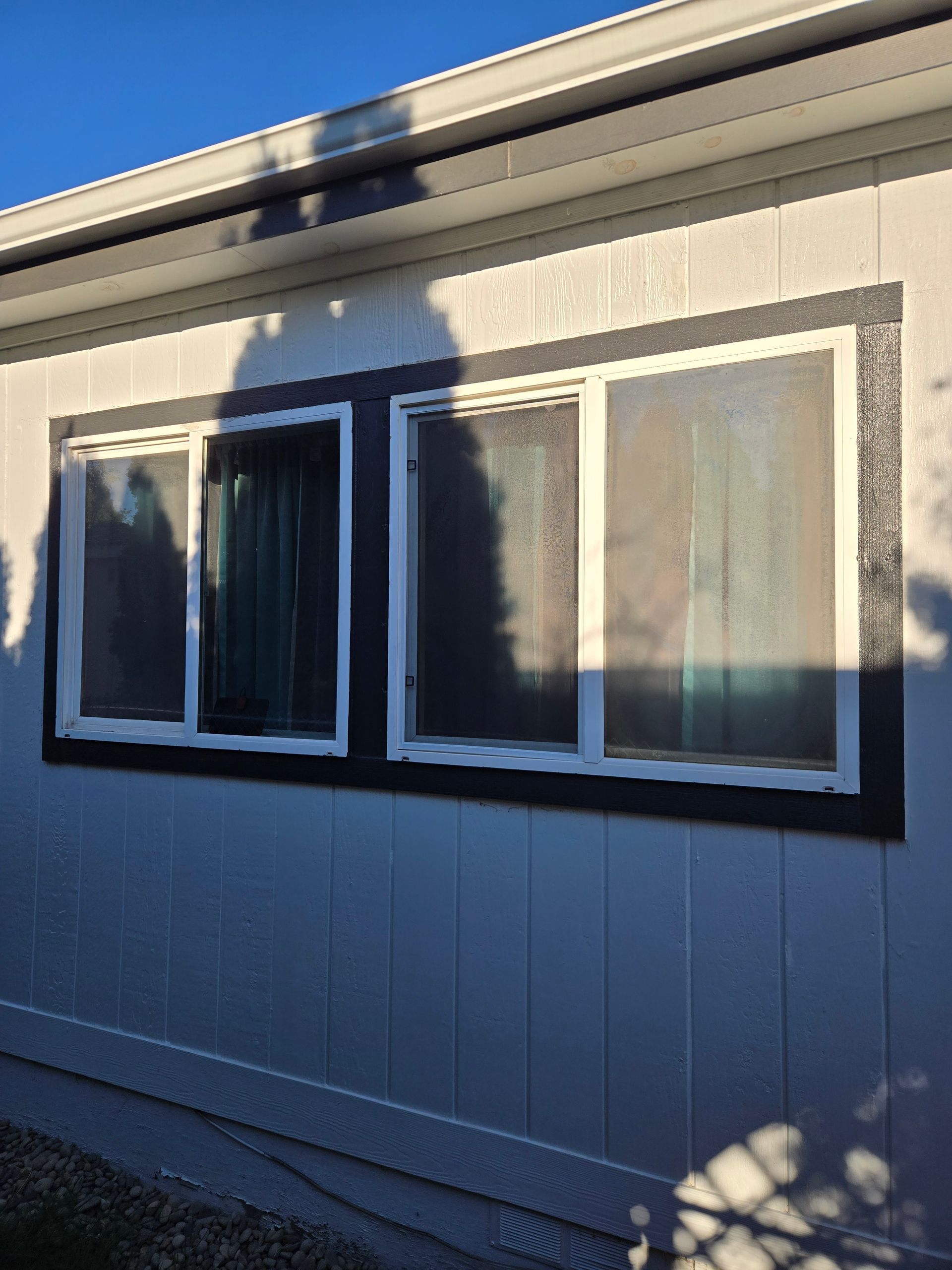 Exterior wall with two windows, white trim, and sunlight casting shadows on the siding.