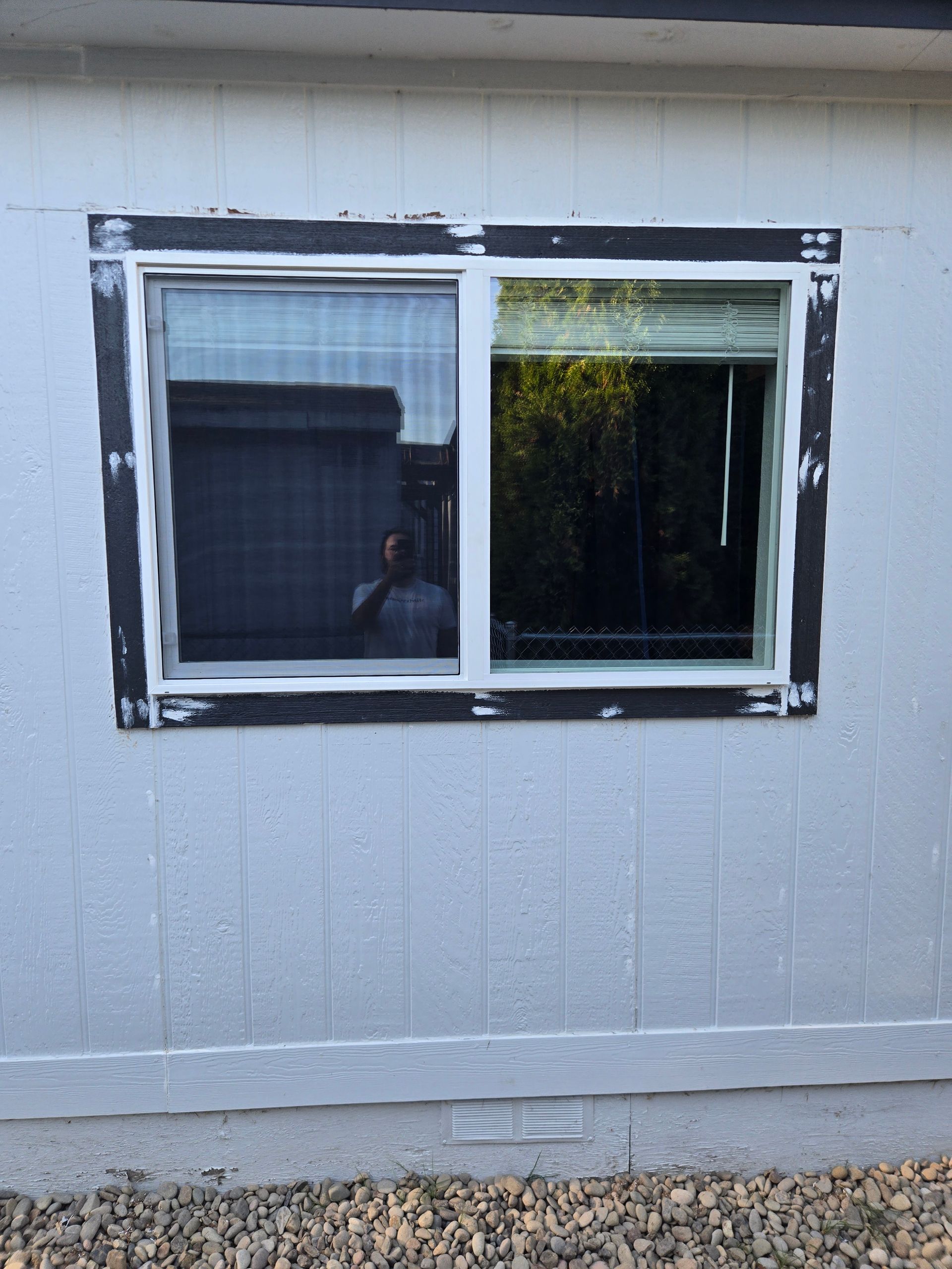White exterior wall with a double-pane sliding window, one pane open and dark reflections in the glass.