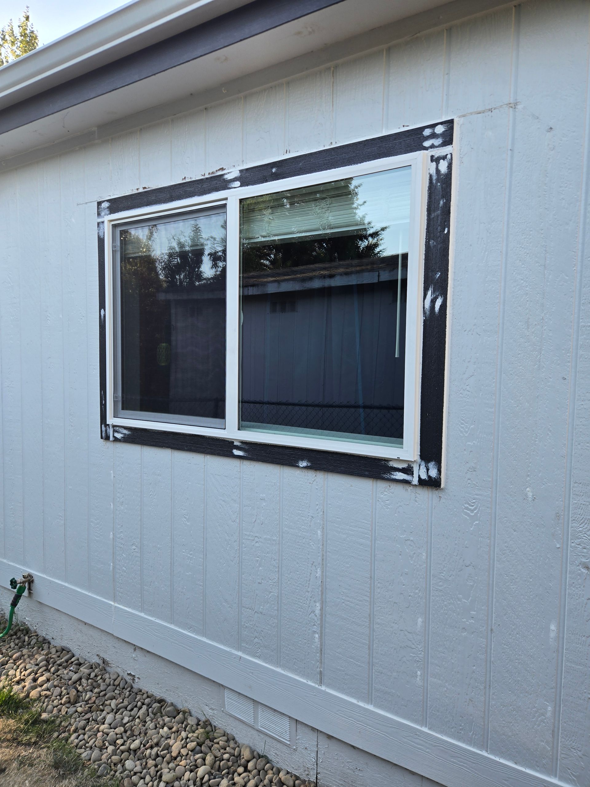 White house exterior with a window framed by taped-up trim and unfinished siding