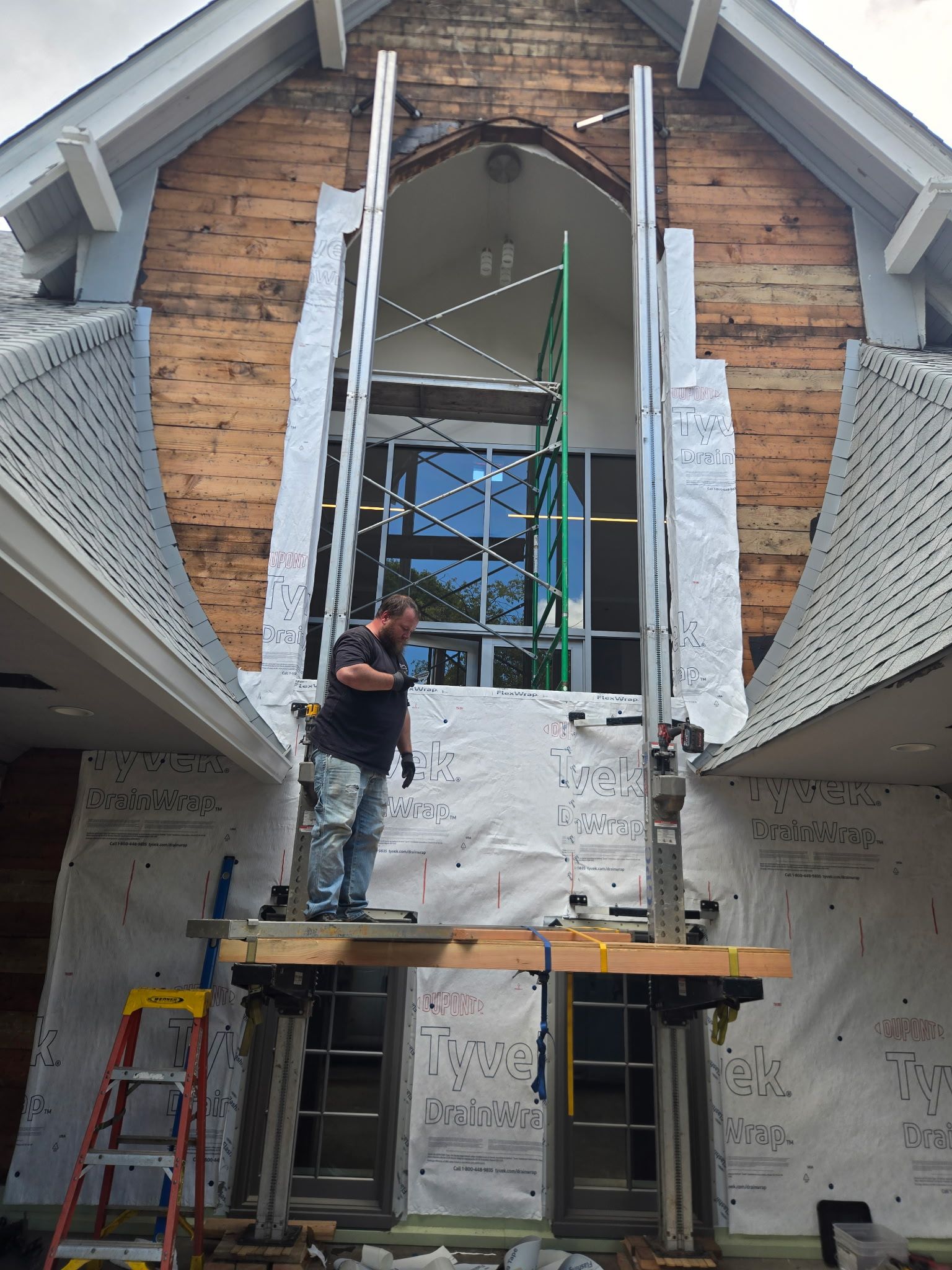 Worker on scaffolding at a partially open building facade with exposed wood and metal supports.