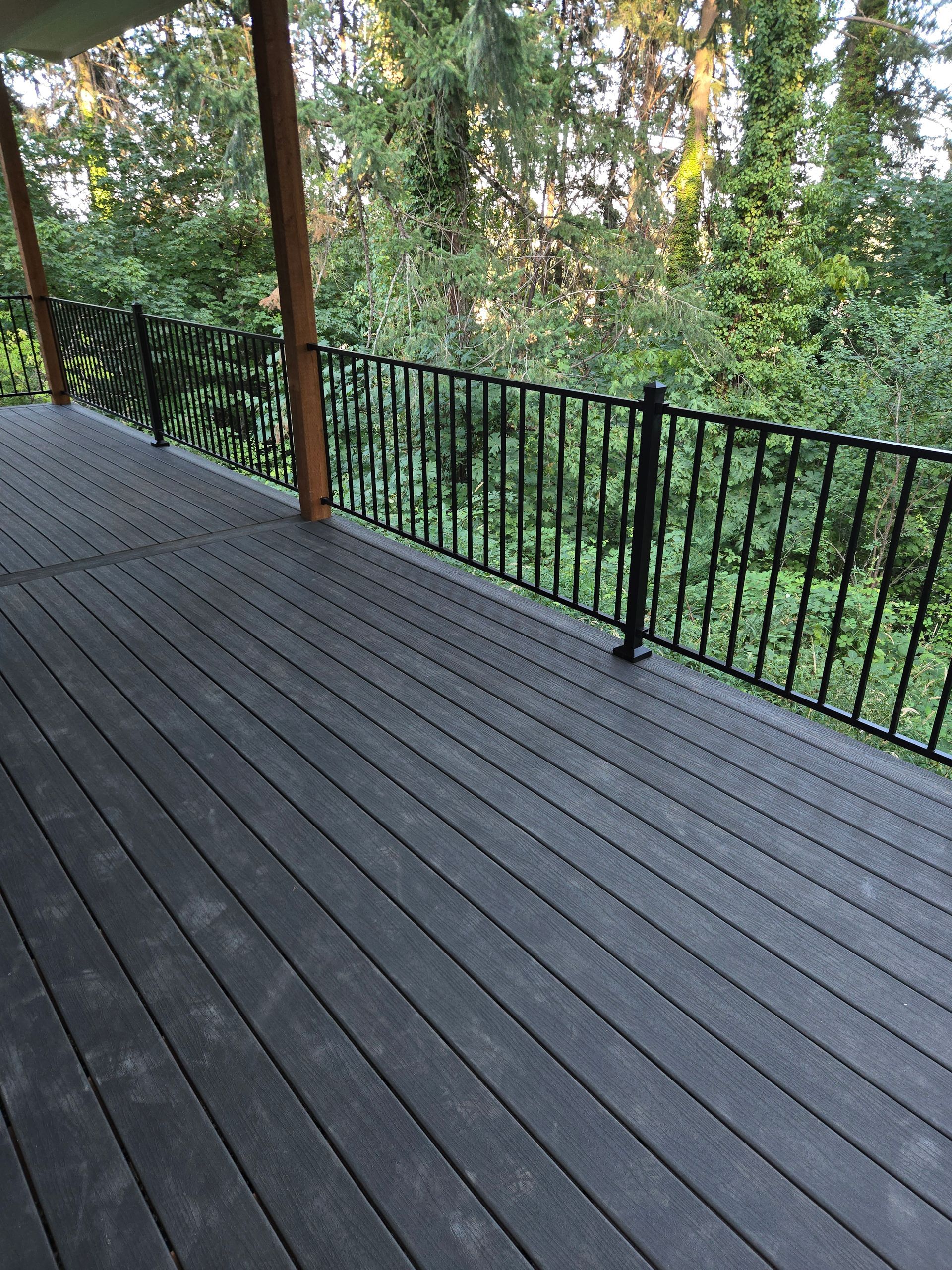 Wooden deck with black railing overlooking a wooded green hillside