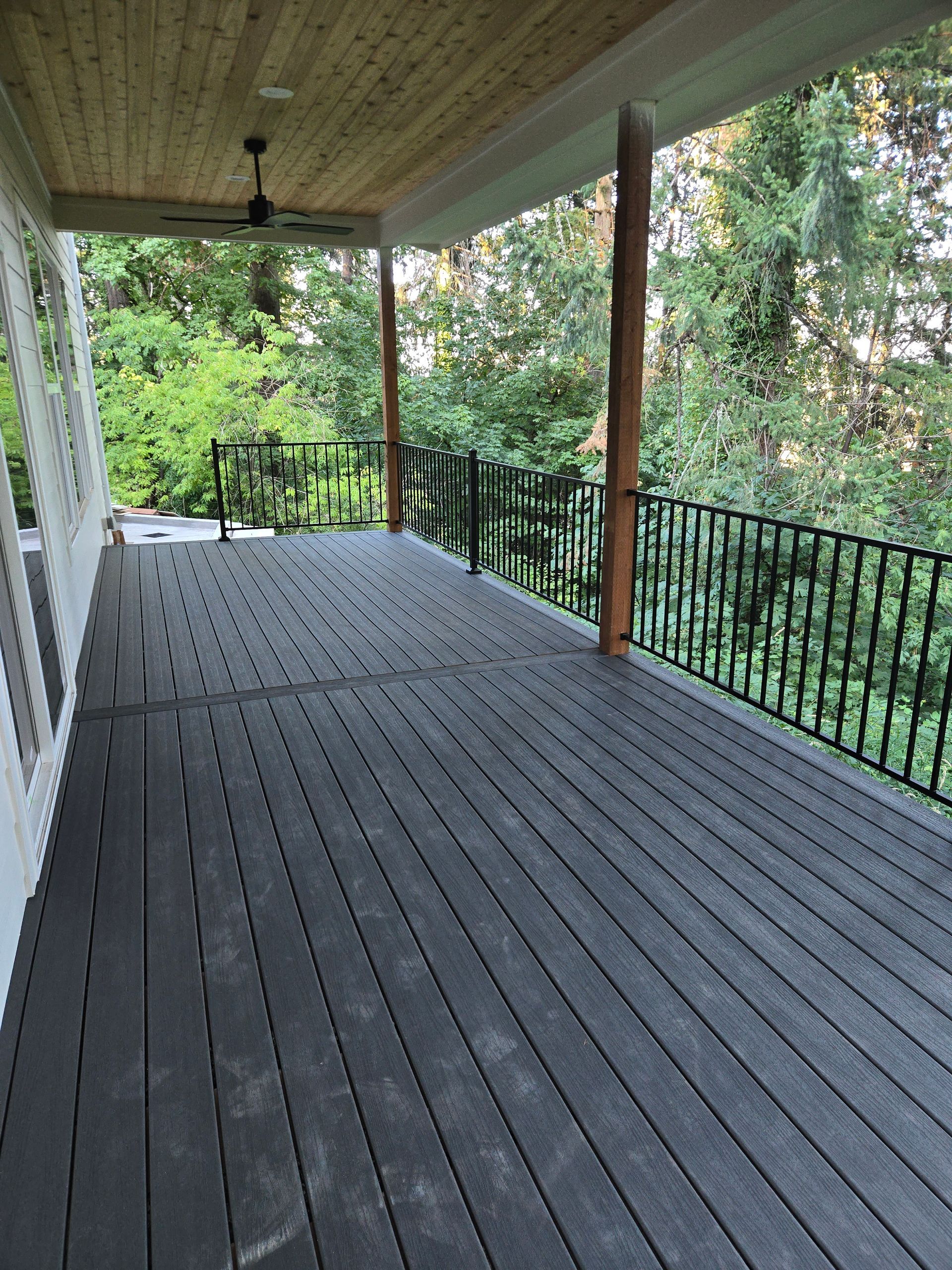 Covered wooden porch with gray floorboards, railing, and trees visible beyond the deck