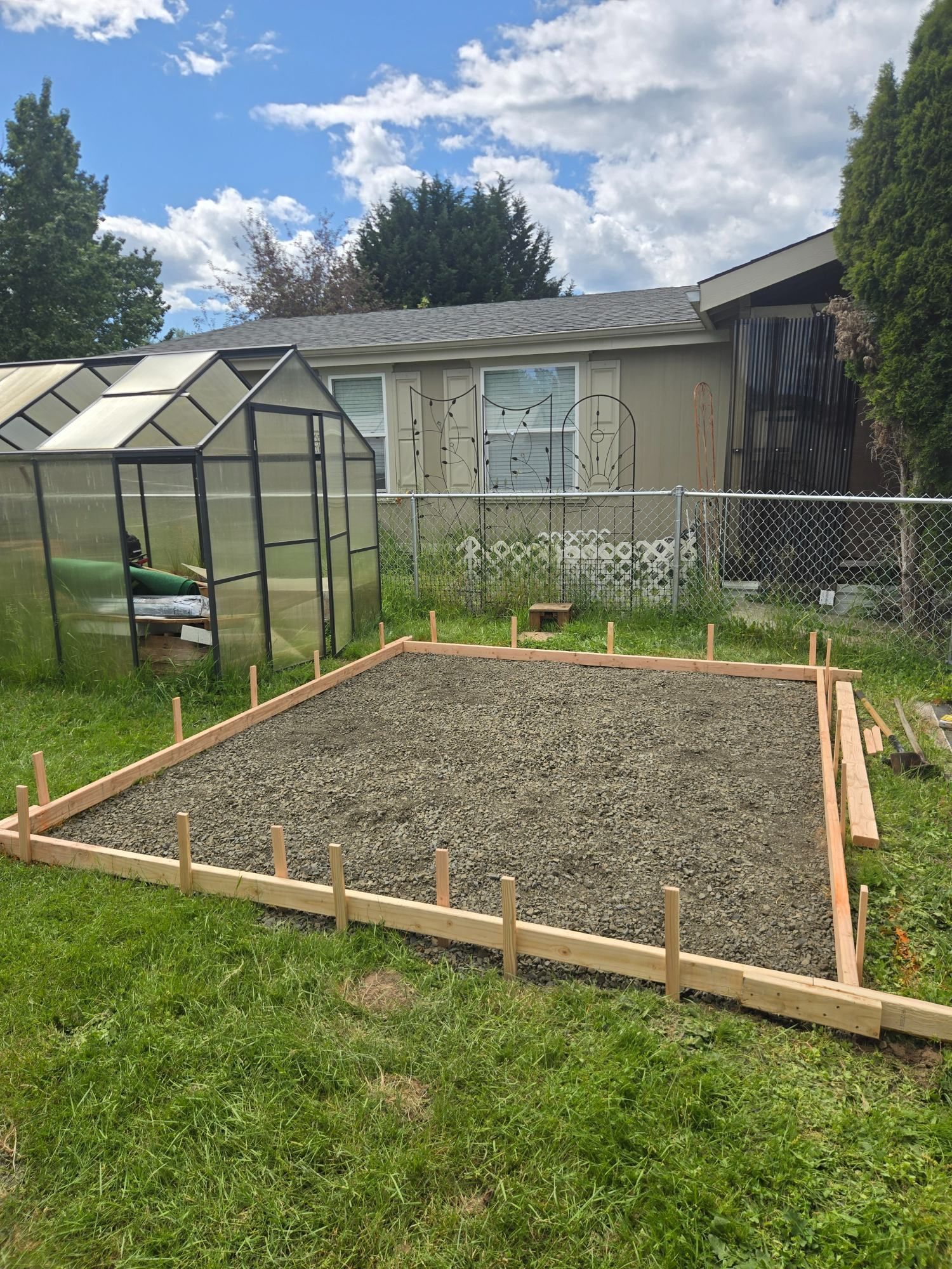 Backyard garden bed with fresh gravel, wooden border, greenhouse, and house in the background