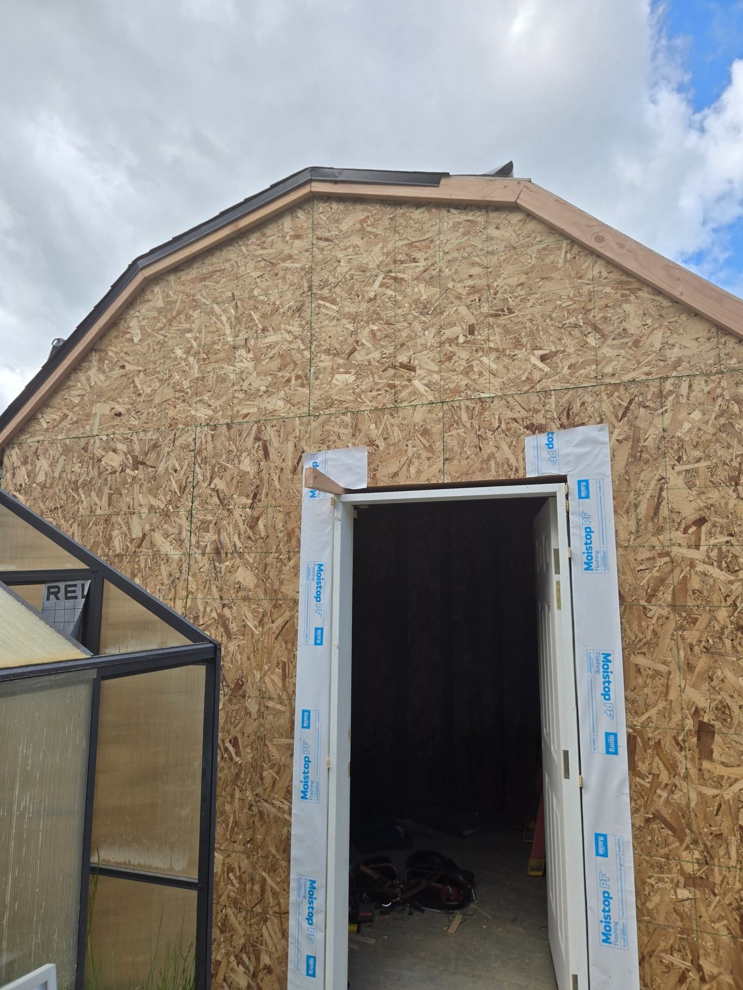Small unfinished shed with OSB siding and open doorway under a cloudy sky