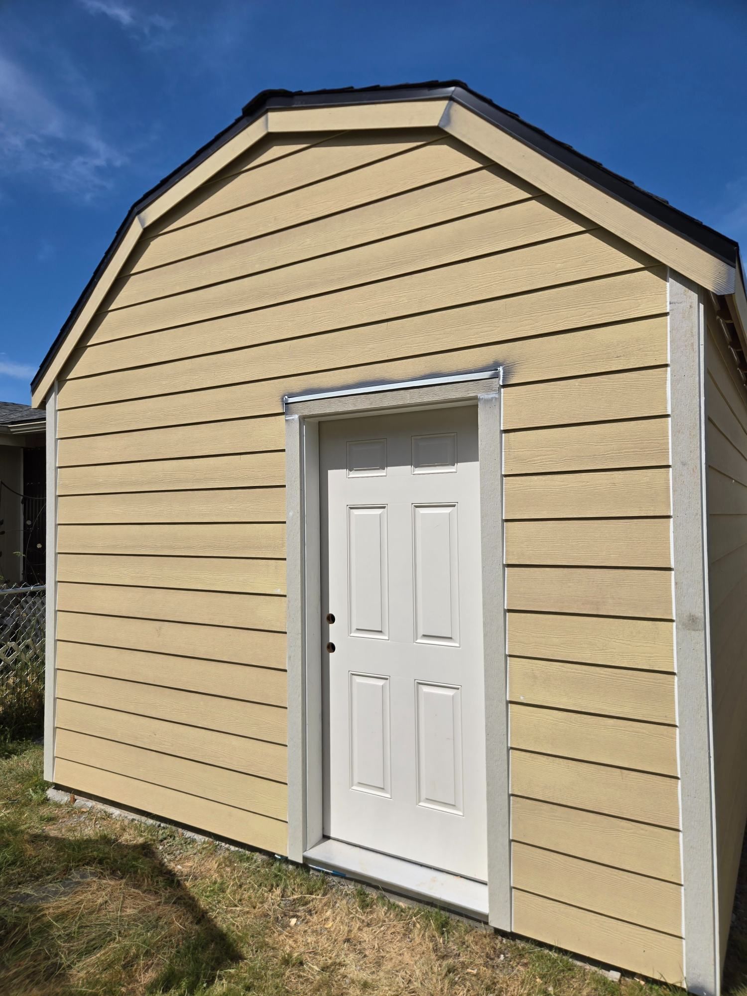 Beige shed with white trim and door against a blue sky
