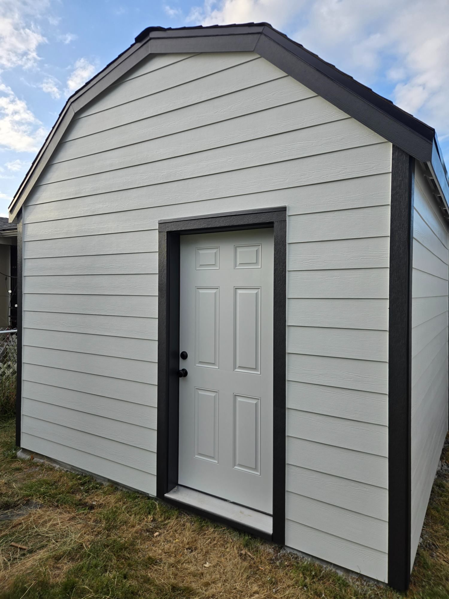 Small white shed with gray trim and a gray door, shown outdoors on grass.