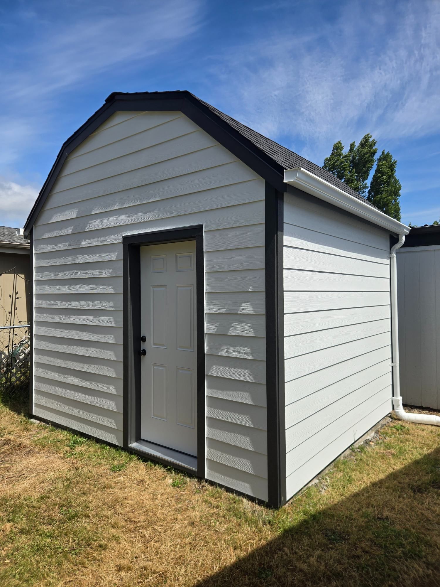 Small gray shed with black trim and a centered door in a sunny backyard