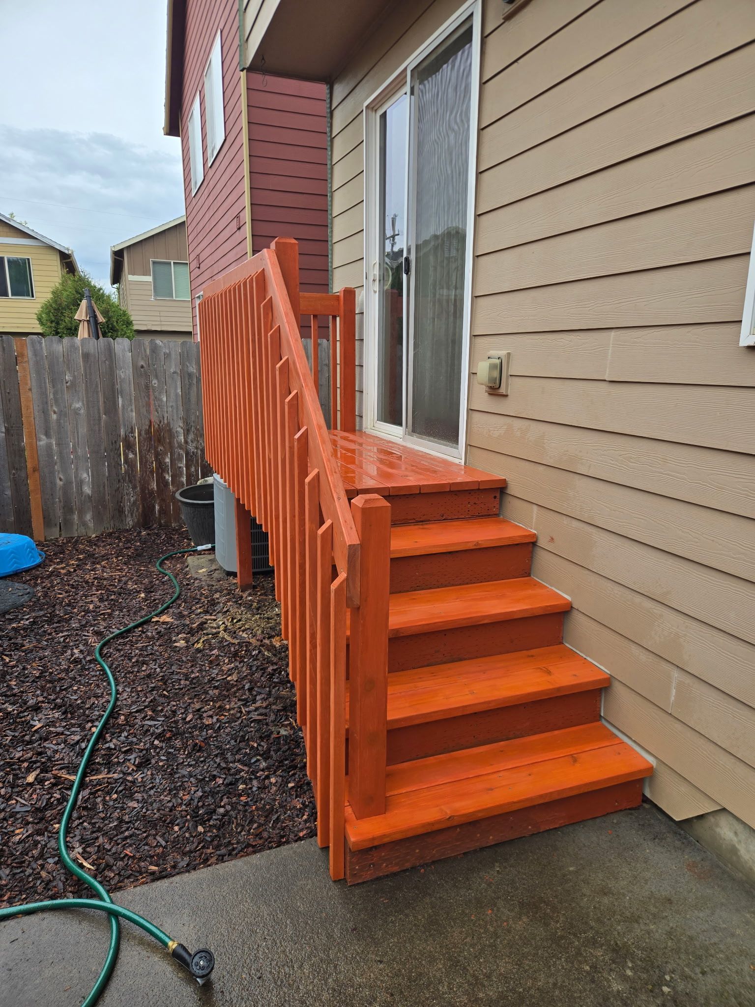 Bright orange wooden stairs with railing leading to a house side door beside a beige exterior wall.