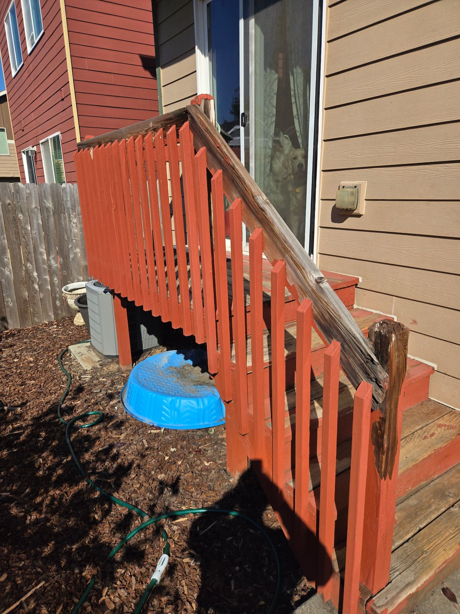 Orange wooden porch railing beside tan siding and brick steps in a backyard.