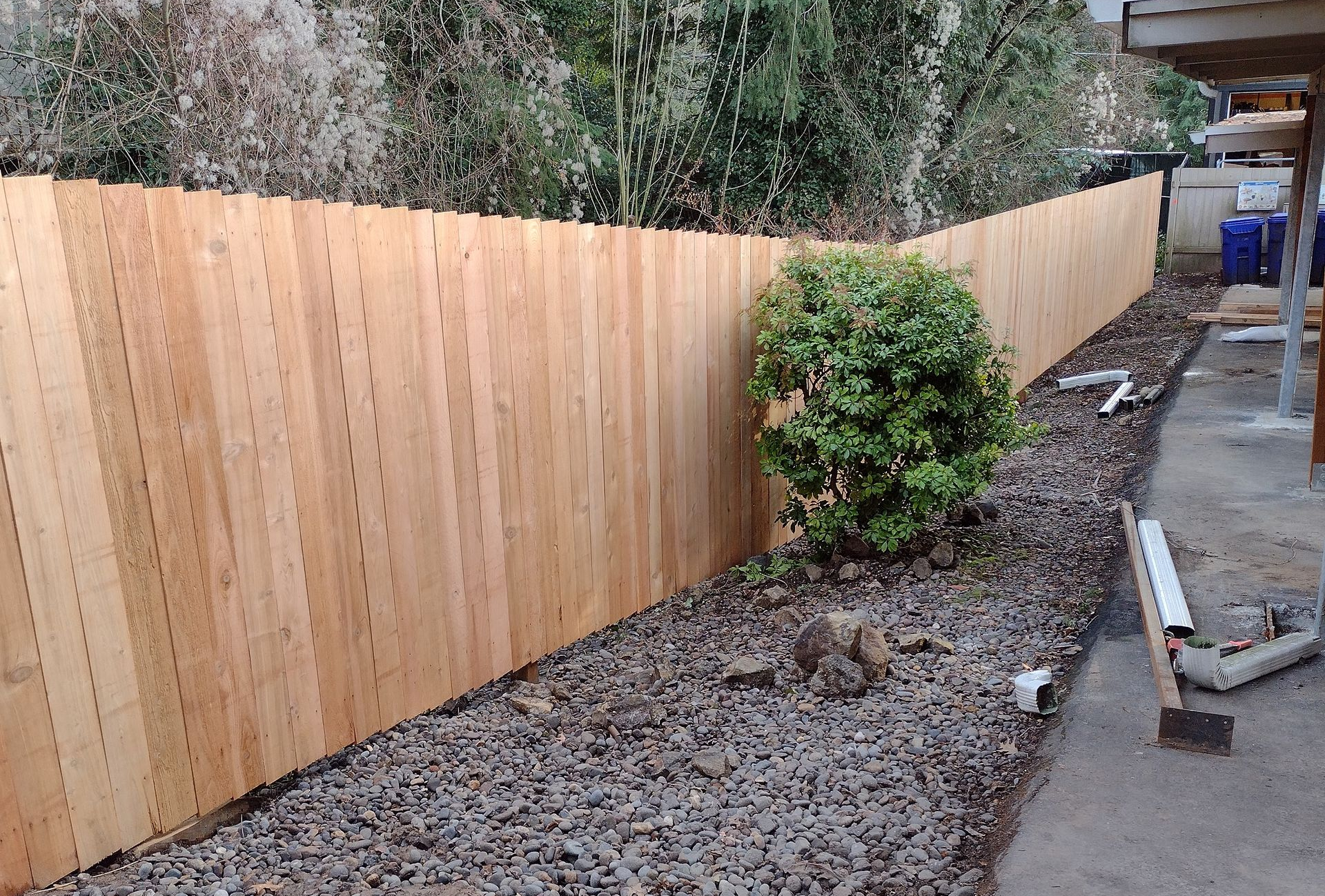Fresh wooden fence along a narrow gravel path beside a shrub and patio area