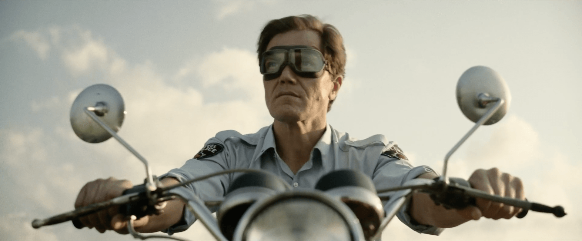 Man wearing sunglasses rides a motorcycle on an open road, seen from the front