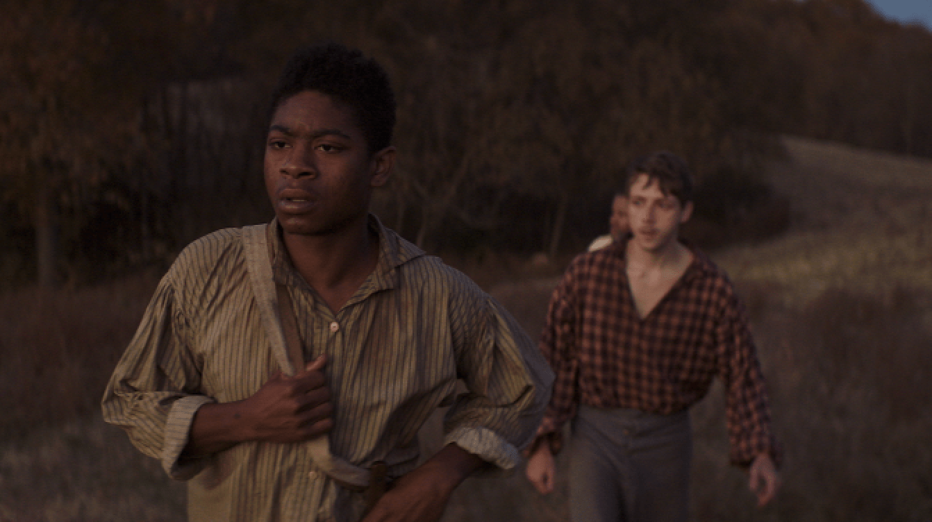 Two runners sprint through a dim, dusty field at dusk.