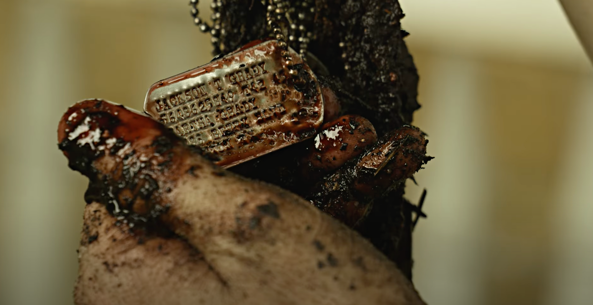 Bloodied hand holding a small orange device against a dark tree trunk
