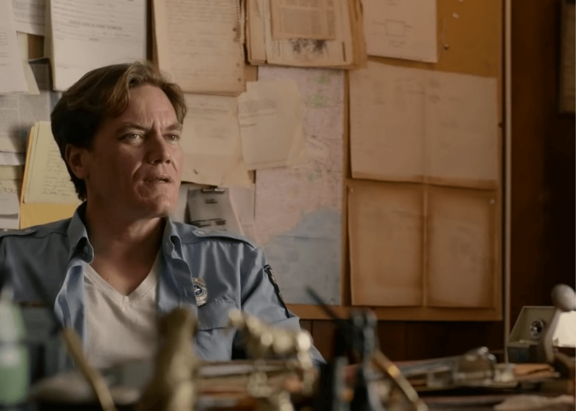 Man sitting in a cluttered office with papers pinned on the wall, looking off to the side.