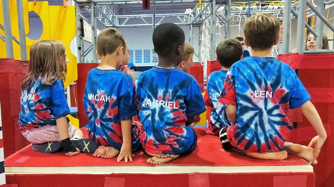 A group of children wearing tie dye shirts are sitting on a red block.