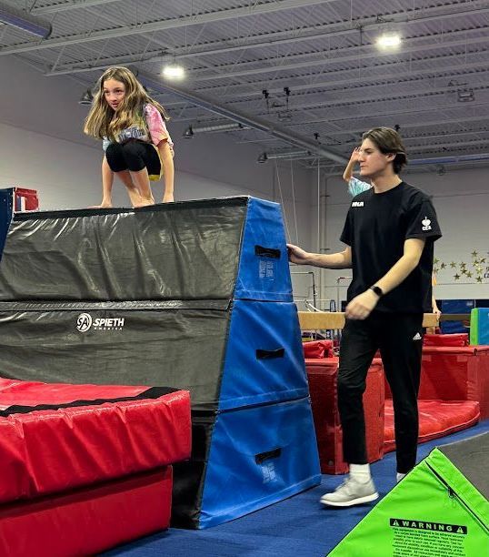 A young girl is doing a handstand on a pyramid while a man watches.
