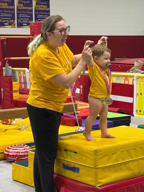 A woman is teaching a baby how to walk on a balance beam.