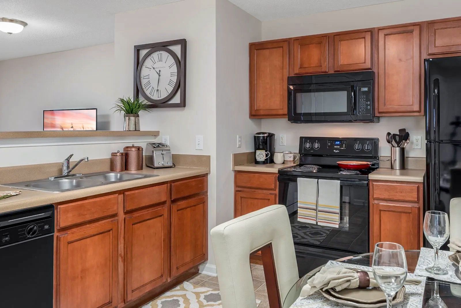 Kitchen with brown cabinets, black appliances, a round clock, and a dining table set for a meal.