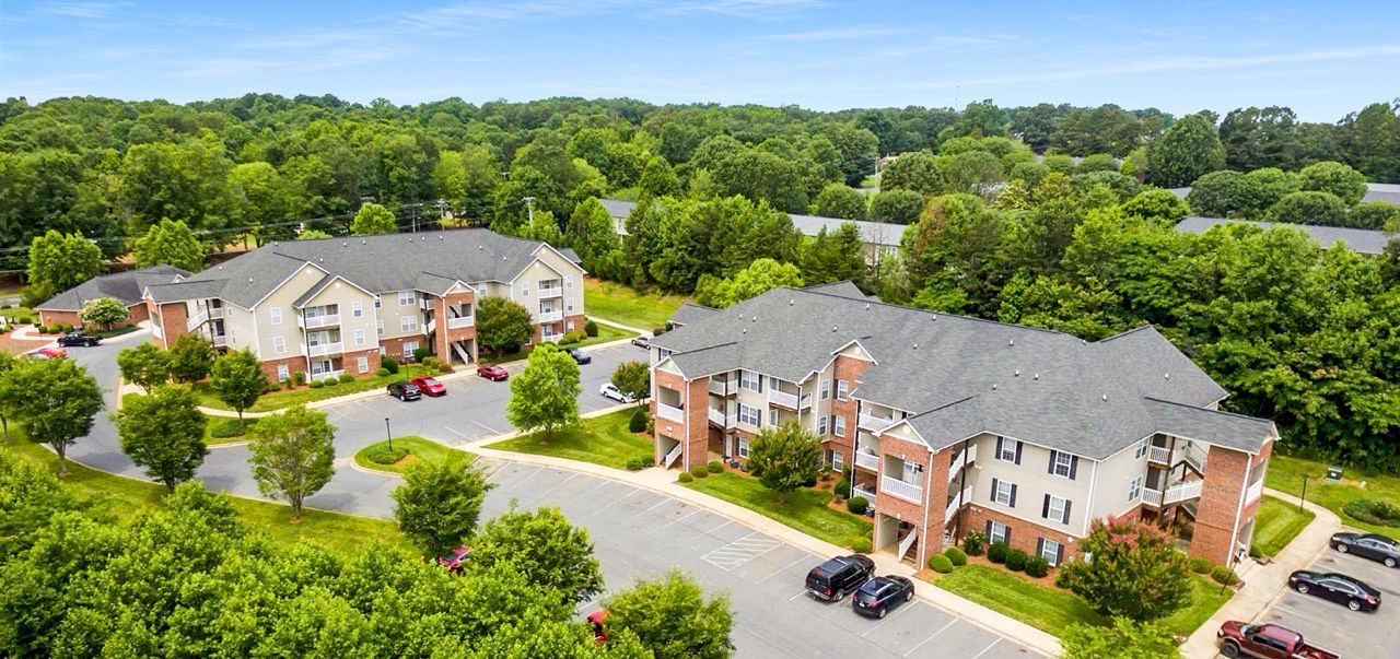 Aerial view of apartment buildings surrounded by trees and a parking lot.
