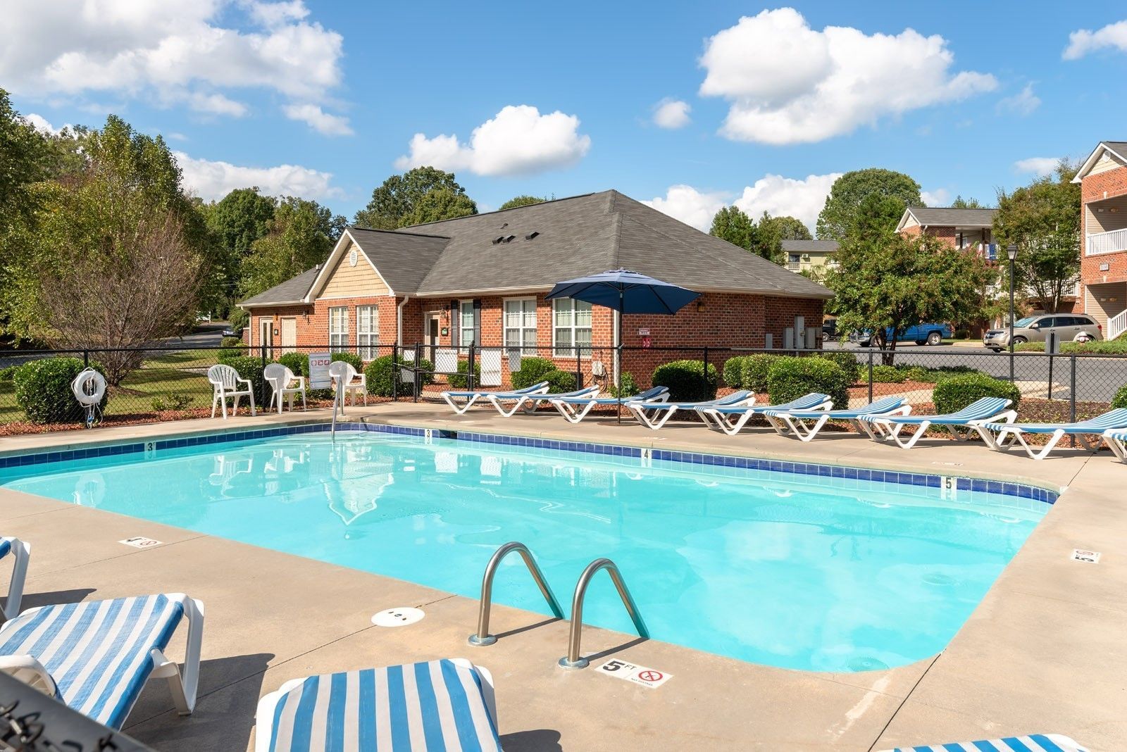 Pool with lounge chairs and building on a sunny day.