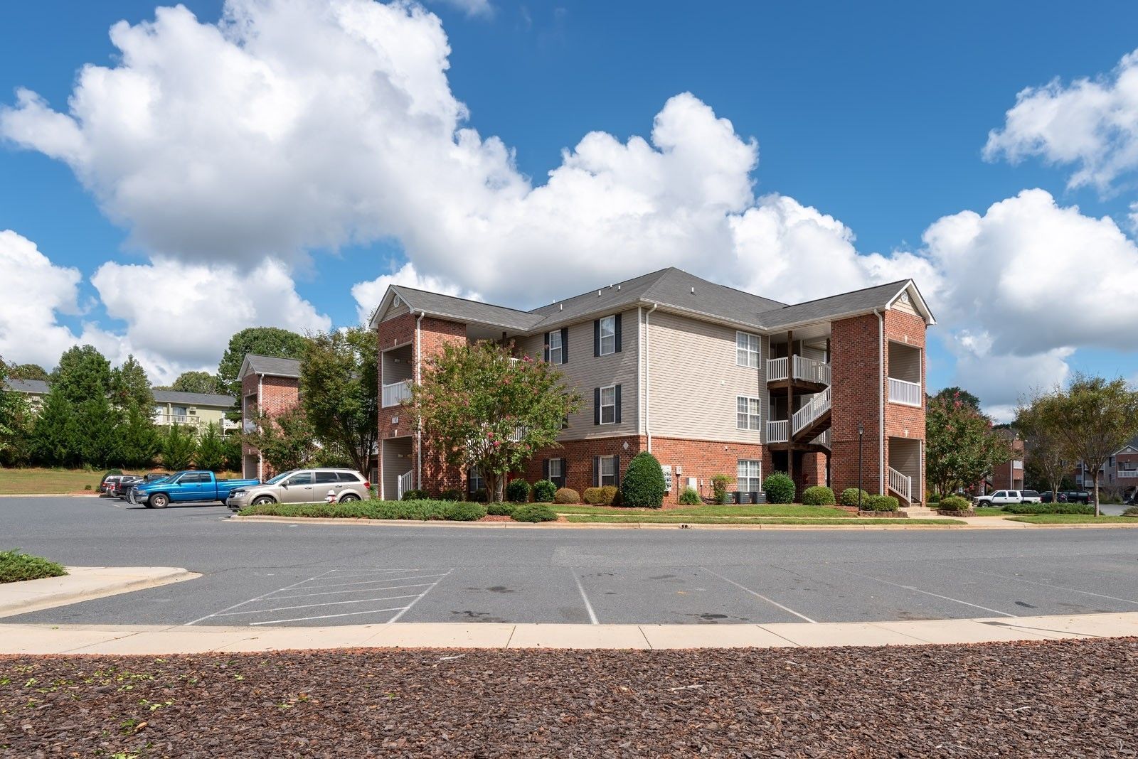 Apartment building with brick accents and balconies on a sunny day with blue sky and puffy clouds.