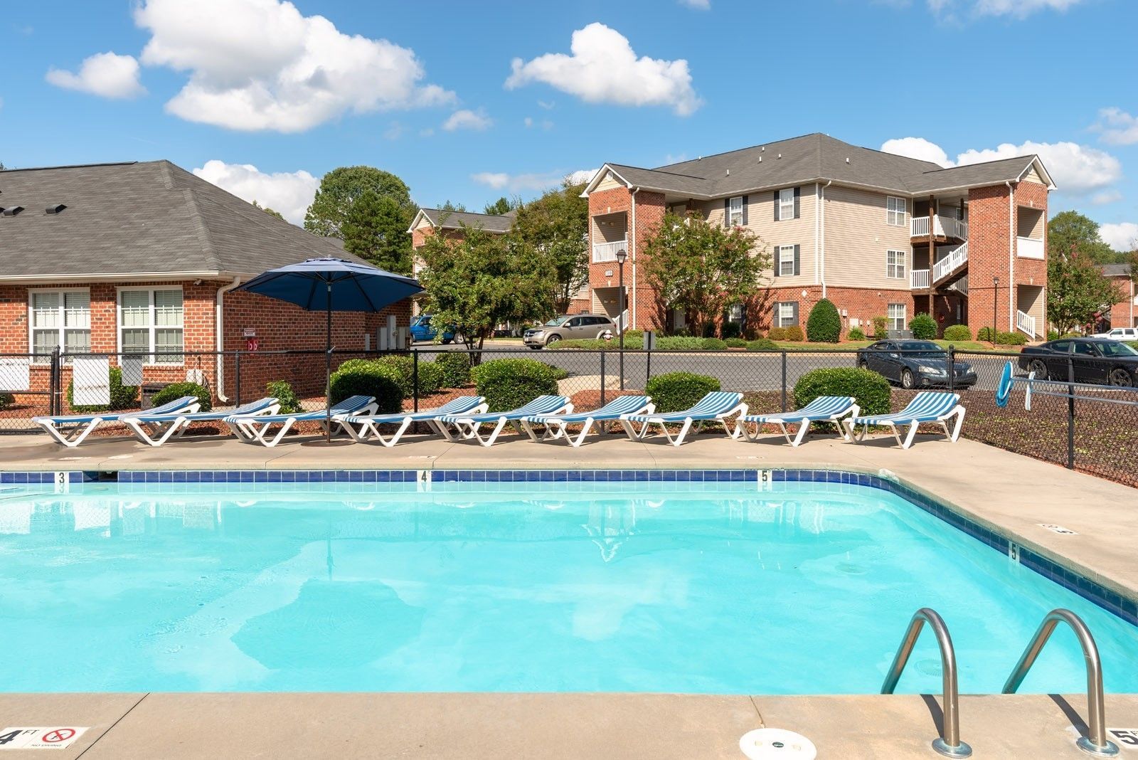 Pool with lounge chairs and apartment buildings in the background on a sunny day.