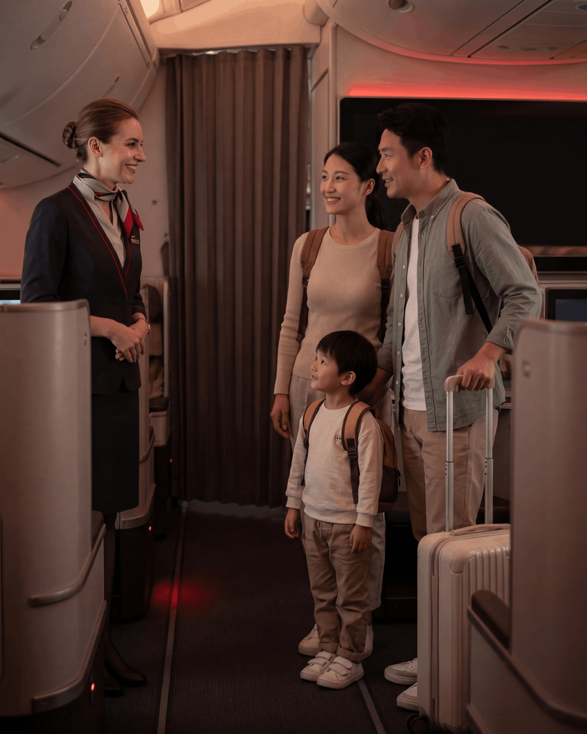 En flyvertinne hilser på en familie med bagasje i en flykabin.