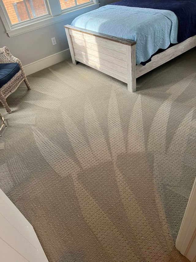 Bedroom with a white bed, blue blanket, and gray carpet near a sunlit window.