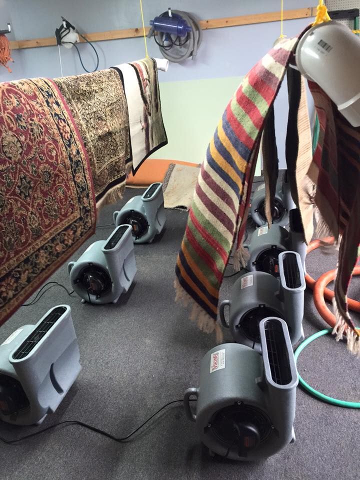 Towels draped over portable floor fans in a small room, with hoses and a wall-mounted fan nearby.
