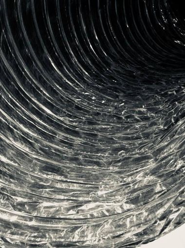 Looking up inside a shiny corrugated metal pipe with a dark opening and bright reflections