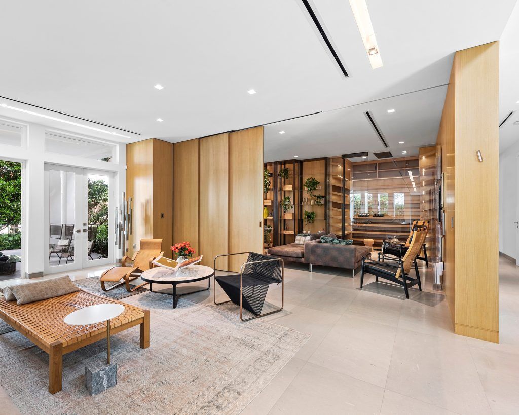 Modern open-plan living room with light wood panels, white walls, and neutral seating around a coffee table.