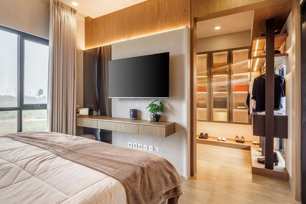 Modern bedroom with a wall-mounted TV, beige bed, and open closet area with warm lighting