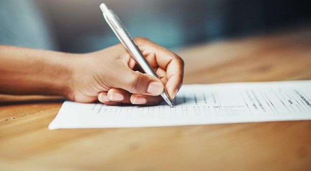 Hand writing with a pen on a white sheet of paper on a wooden table