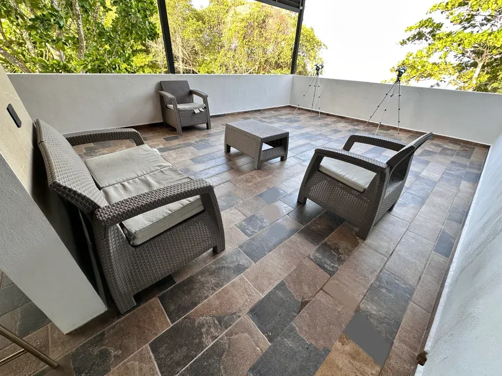 Patio exterior con muebles de mimbre marrón y suelo de baldosas.