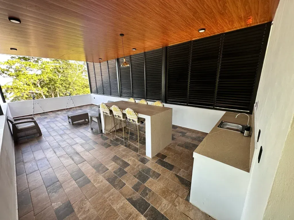 Patio exterior con cocina, barra, asientos y panel de privacidad de listones. Tonos marrones y blancos.
