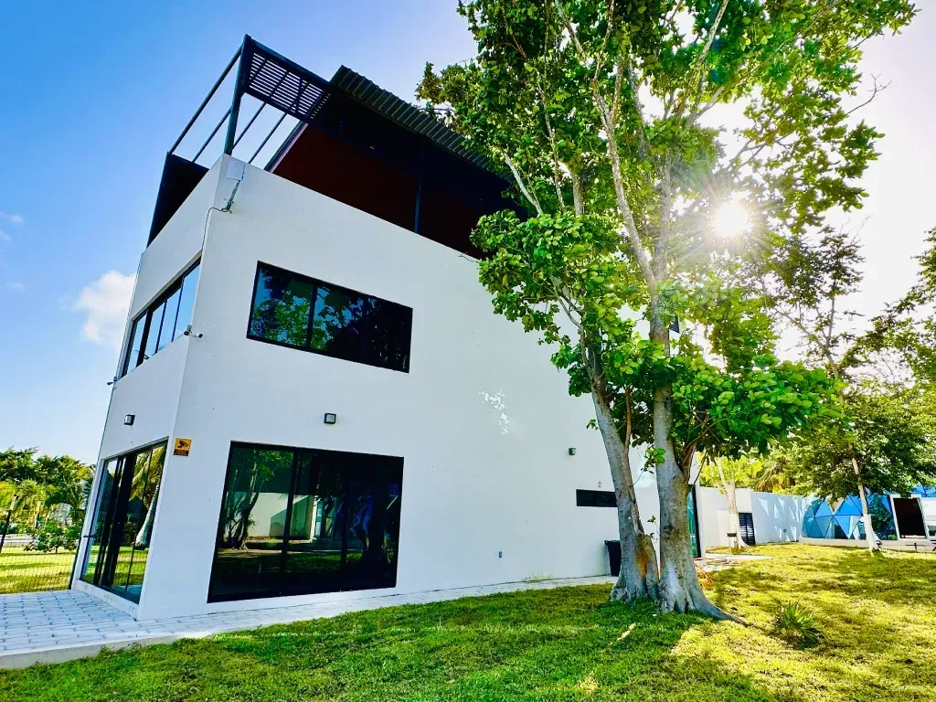 Edificio moderno de tres plantas, de color blanco, con grandes ventanales y terraza en la azotea,.
